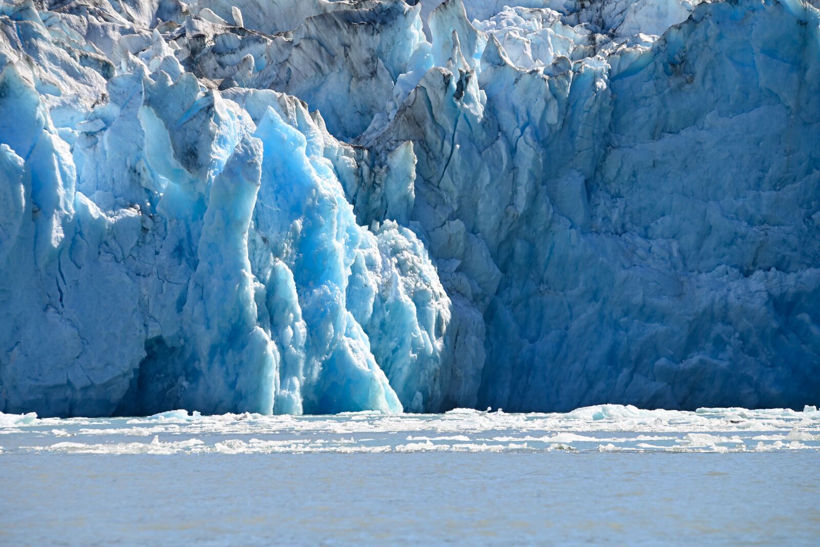 Blue tidewater glacier face in Alaska calving into the sea